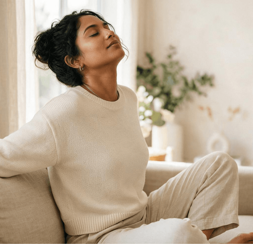 A relaxed woman in a cream sweater stretching on a sofa in soft daylight