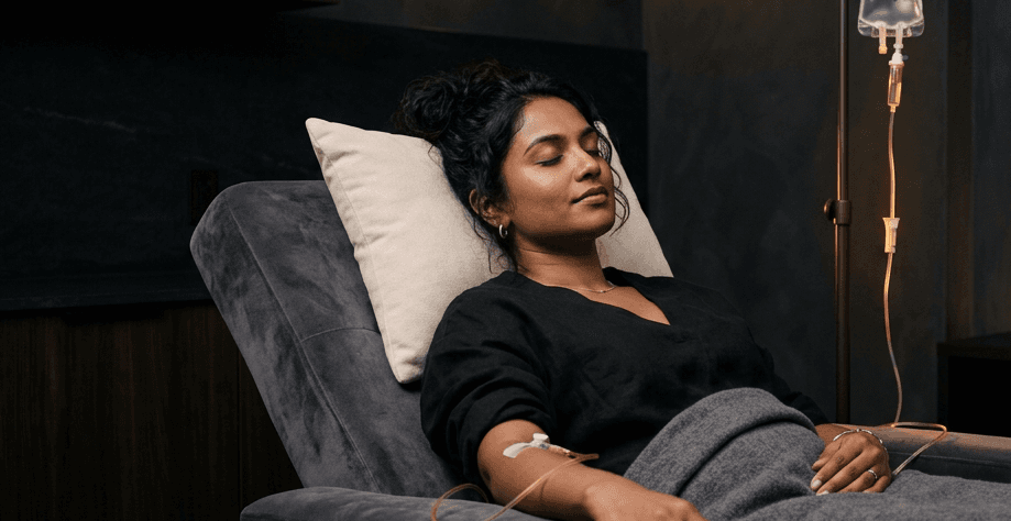 A patient reclining in a dim luxury lounge while receiving an IV infusion