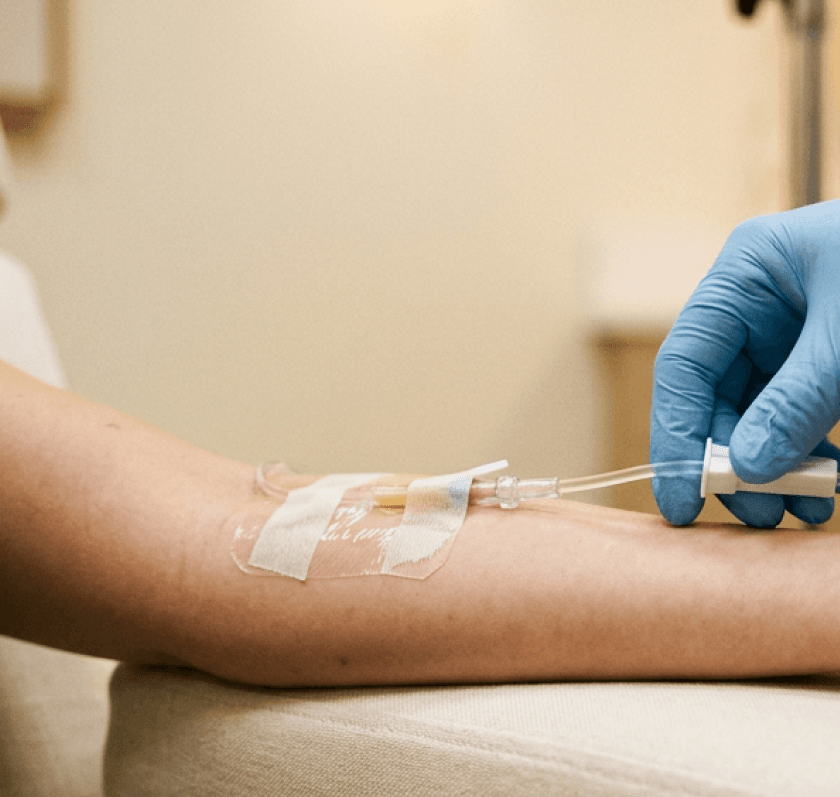 A clinician in blue gloves adjusting an IV line in a patient's arm