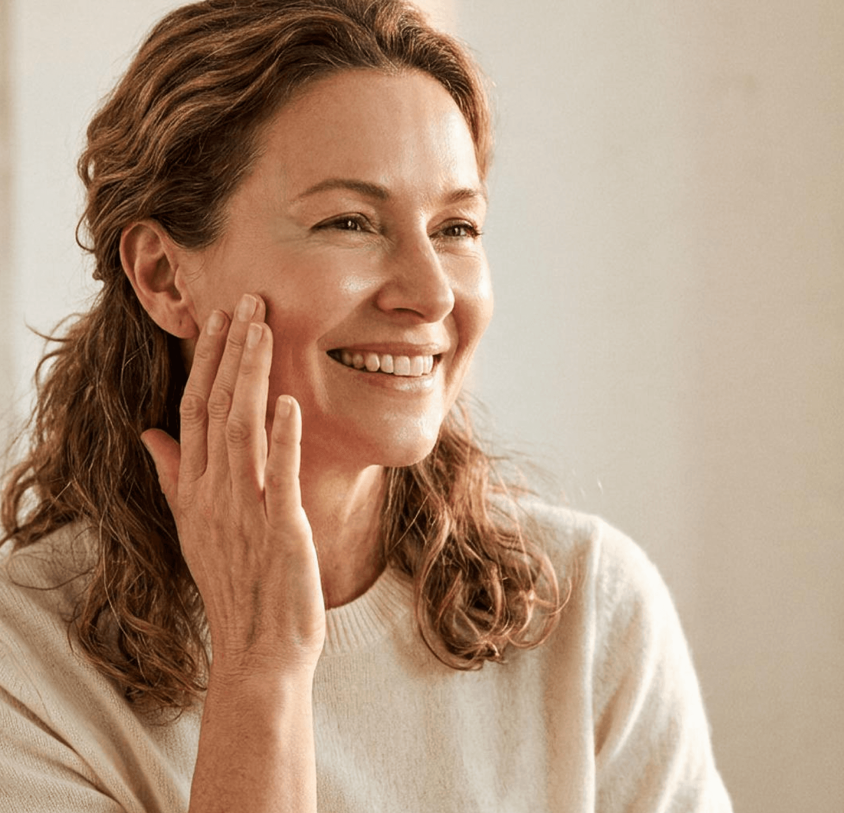 A smiling woman touching her cheek with radiant skin