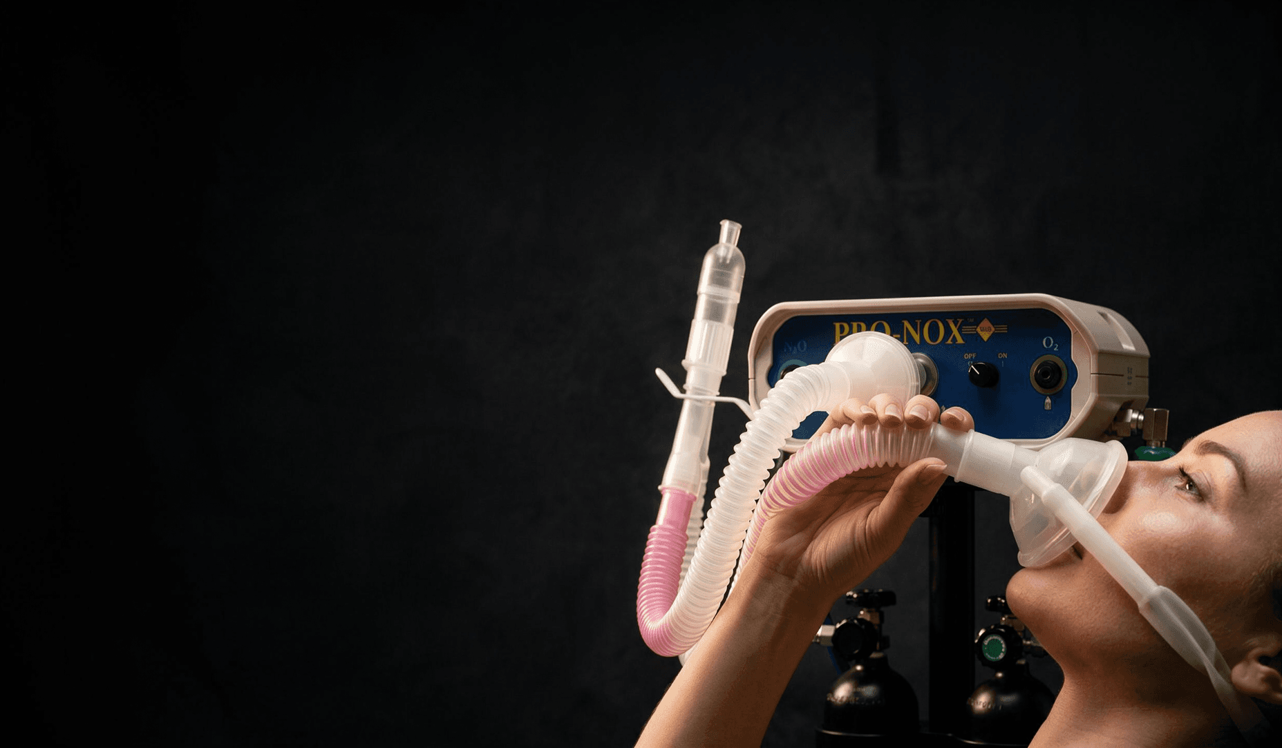 Hands holding the Pro-Nox breathing circuit and mask in front of the unit's control panel